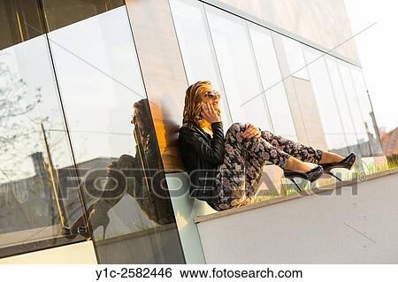 Stock Photograph - Fanciful young lady sitting talking on cellphone. Fotosearch