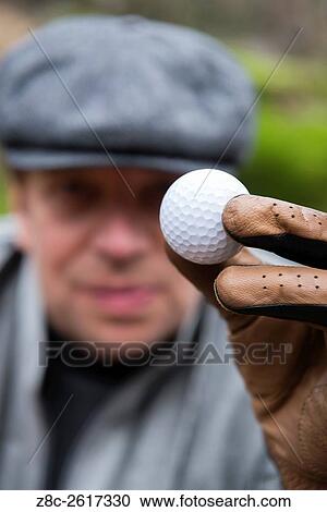 Golfer with flat cap and a glove holding up a golf ball in Ascona, Switzerland. View Large Photo Image Stock Image - Golfer with flat cap and a glove holding up a golf ball in Ascona, Switzerland.. Fotosearch