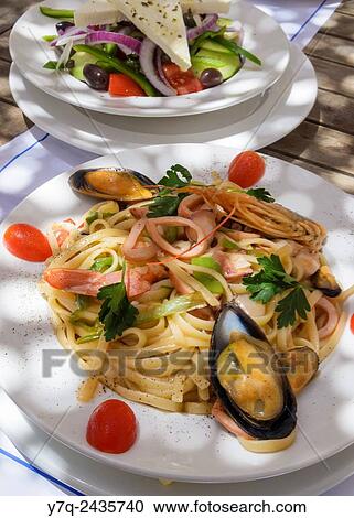 Stock Image - Greek Linguine di Mare and Greek salad, on the island of Paros, Greece.. Fotosearch