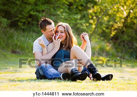 Stock Image - Happy young couple sitting on the grass. Fotosearch