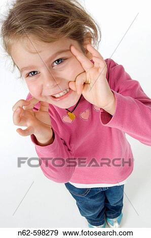 Little girl with happy facial expression pinches her cheek with one hand and the other puts it close to the face View Large Photo Image Stock Photo - Little girl with happy facial expression pinches her cheek with one hand and the other puts it close to the face. Fotosearch