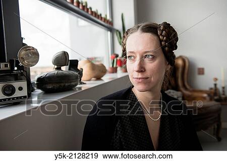 Stock Photo - Living room or salon of studio apartment, Eindhoven, Netherlands. Young, attractive woman with tresses and tails in her hear, wearing a pearl neckless inherited from her grandmother.. Fotosearch