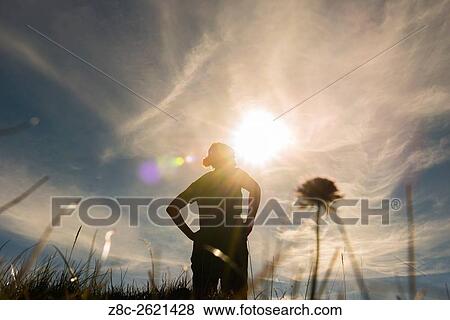 Stock Photo - Low angle view on a proud woman in backlit with sunshine and grass and flower in Grisons, Switzerland.. Fotosearch