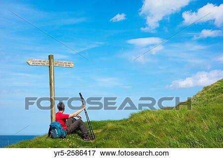 Male hiker on The Cleveland Way National Trail coastal footpath resting near signpost at Skinningrove, North Yorkshire, England, United Kingdom. View Large Photo Image Stock Photo - Male hiker on The Cleveland Way National Trail coastal footpath resting near signpost at Skinningrove, North Yorkshire, England, United Kingdom.. Fotosearch