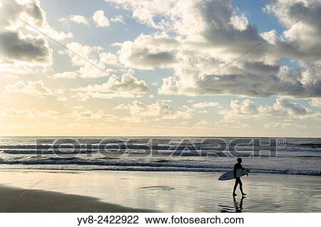 Stock Image - Male surfer walking at the beach at sunset, La Jolla, California.. Fotosearch