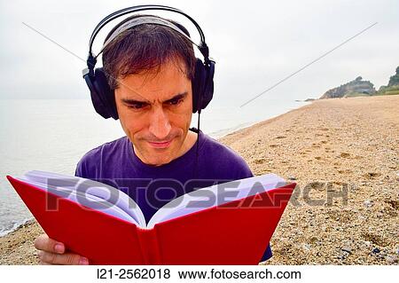 Man is reading a book in a beach while he is listening music with his headphones. View Large Photo Image Stock Photo - Man is reading a book in a beach while he is listening music with his headphones.. Fotosearch