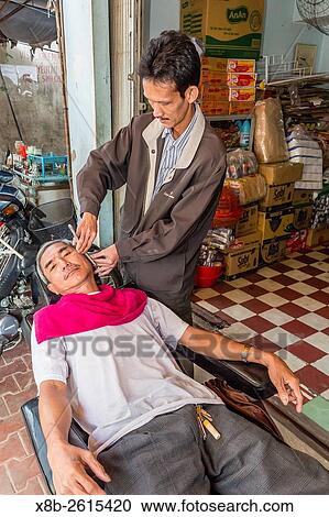 Stock Image - Man receiving a shave at the local market in Chau Doc, Mekong River Delta, Vietnam.. Fotosearch