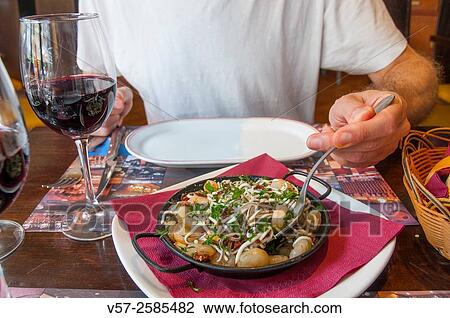 Stock Image - Man serving a dish of eels with prawns.. Fotosearch