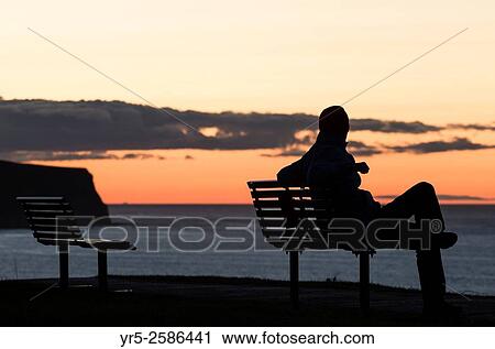 Man sitting on seat overlooking North Sea at sunset at Whitby, North Yorkshire, England, United Kingdom. View Large Photo Image Stock Image - Man sitting on seat overlooking North Sea at sunset at Whitby, North Yorkshire, England, United Kingdom.. Fotosearch