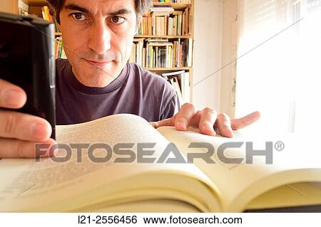 Man using his mobile phone while he is reading a book in an interior, room of a house. View Large Photo Image Stock Photograph - Man using his mobile phone while he is reading a book in an interior, room of a house.. Fotosearch