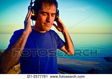 Man with blue t-shirt is listening music with his headphones on outdoor near the sea. View Large Photo Image Stock Image - Man with blue t-shirt is listening music with his headphones on outdoor near the sea.. Fotosearch