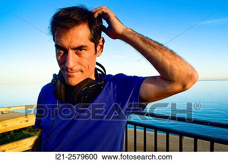 Man with headphones hanging on the neck behind a railing near the sea. He is wearing a blue t-shirt. View Large Photo Image Stock Image - Man with headphones hanging on the neck behind a railing near the sea. He is wearing a blue t-shirt.. Fotosearch