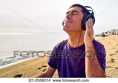 Man with headphones listening to music on a beach, near the sea. View Large Photo Image Picture - Man with headphones listening to music on a beach, near the sea.. Fotosearch