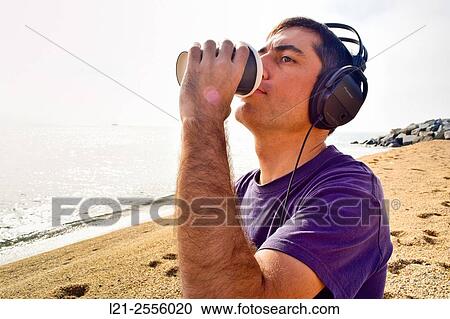 Man with headphones listening to music while he is drinking coffee with a disposable cup on a beach, near the sea. View Large Photo Image Stock Image - Man with headphones listening to music while he is drinking coffee with a disposable cup on a beach, near the sea.. Fotosearch