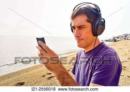 Man with headphones listening to music while he is using a mobile phone on a beach, near the sea. View Large Photo Image Stock Photo - Man with headphones listening to music while he is using a mobile phone on a beach, near the sea.. Fotosearch