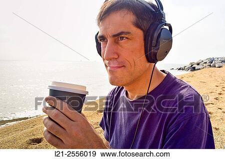 Man with headphones listening to music while he is holding a disposable cup of coffee on a beach, near the sea. View Large Photo Image Stock Photo - Man with headphones listening to music while he is holding a disposable cup of coffee on a beach, near the sea.. Fotosearch