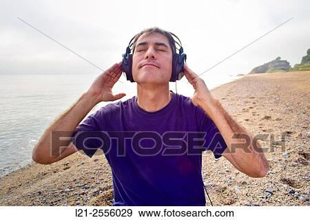 Man with headphones listening to music on a beach, near the sea. View Large Photo Image Stock Photo - Man with headphones listening to music on a beach, near the sea.. Fotosearch