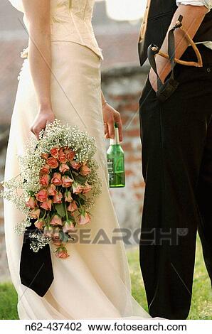 Married couple, she is holding the bouquet and a bottle of beer, he has a slingshot in his pocket View Large Photo Image Stock Image - Married couple, she is holding the bouquet and a bottle of beer, he has a slingshot in his pocket. Fotosearch
