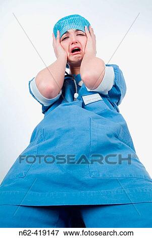 Stock Photo - Nurse with blue uniform puts her hands around her head to express despair. Fotosearch