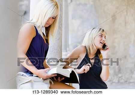 Stock Image - One girl is studying another is talking on the cellular phone. Fotosearch