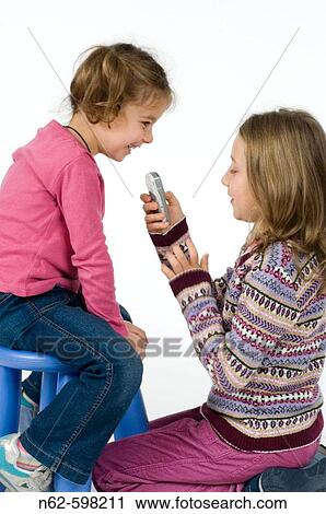 Pair of little girls playing with a cell phone the younger is sitting on a stool and the other is kneeling on the floor View Large Photo Image Stock Image - Pair of little girls playing with a cell phone the younger is sitting on a stool and the other is kneeling on the floor. Fotosearch
