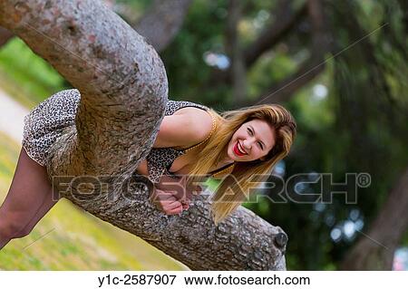 Stock Photo - Playful young woman bending over tree trunk. Fotosearch