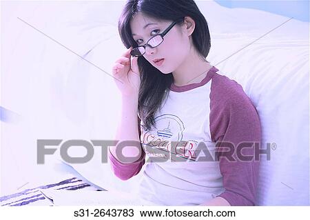 Stock Image - portrait of a beautiful young asian girl from canada reading a book sitting on the floor.. Fotosearch