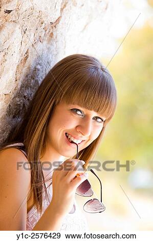 Stock Photo - Portrait of smiling teenager girl with sunglasses in hand. Fotosearch