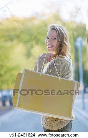 Pretty blonde woman smiling at camera with shopping bag View Large Photo Image Picture - Pretty blonde woman smiling at camera with shopping bag. Fotosearch
