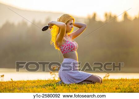 Stock Image - Pretty young woman brushing hair under sunset golden light. Fotosearch