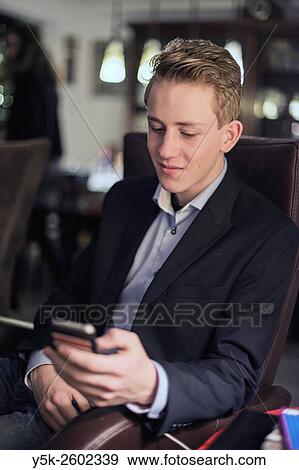 Ridderkerk, Netherlands. Portrait of a young, teenage male sitting in a living room chair during Christmas eve, while playing with his smartphone. View Large Photo Image Stock Photo - Ridderkerk, Netherlands. Portrait of a young, teenage male sitting in a living room chair during Christmas eve, while playing with his smartphone.. Fotosearch