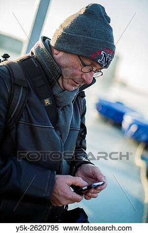Rotterdam, Netherlands. Middle aged man wearing glasses and cap communicating with his martphone. View Large Photo Image Stock Photography - Rotterdam, Netherlands. Middle aged man wearing glasses and cap communicating with his martphone.. Fotosearch