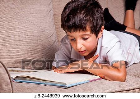 Stock Photo - Schoolboy reading library book at home.. Fotosearch