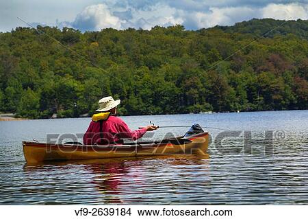 Senior man fishing from a small canoe on Limekiln Lake in Old Forge, New York. Hes in the middle of a cast. View Large Photo Image Picture - Senior man fishing from a small canoe on Limekiln Lake in Old Forge, New York. Hes in the middle of a cast.. Fotosearch
