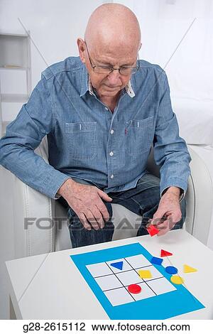 Stock Image - Senior man playing with a psychological test game to detect Alzheimer disease at home. Fotosearch