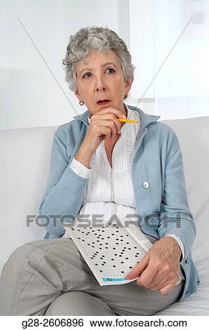 Senior woman with grey hair, busy making a crossword, thoughtful, pen in hand View Large Photo Image Stock Photograph - Senior woman with grey hair, busy making a crossword, thoughtful, pen in hand. Fotosearch