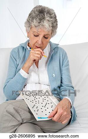 Stock Photography - Senior woman with grey hair, busy making a crossword, thoughtful, pen in hand. Fotosearch