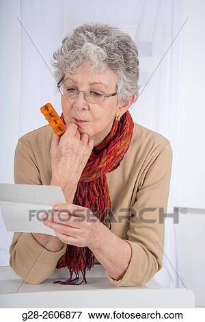 Senior woman with grey hair, holding and reading a prescription, in one hand, and holding a 7 day pill reminder in the other hand View Large Photo Image Stock Photo - Senior woman with grey hair, holding and reading a prescription, in one hand, and holding a 7 day pill reminder in the other hand. Fotosearch