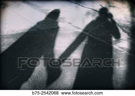 Stock Photo - Shadow of a self portrait of a photographer and his girlfriend holding hands. Regents Park, London, England, UK, Europe.. Fotosearch