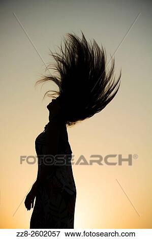 Stock Photo - Silhouette of a young woman flicking hair hair against the sunset.. Fotosearch