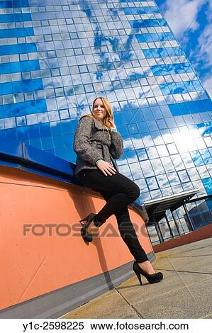 Stock Photography - Tee girl posing before shiny-glass skyscraper house. Fotosearch