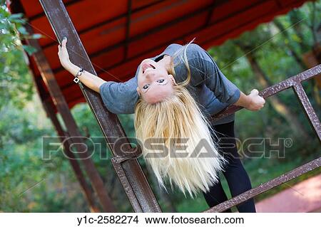 Picture - Teen girl joyful on fence inverted showing tongue. Fotosearch
