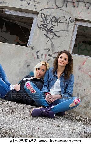 Stock Image - Teen girlfriends sitting on street. Fotosearch