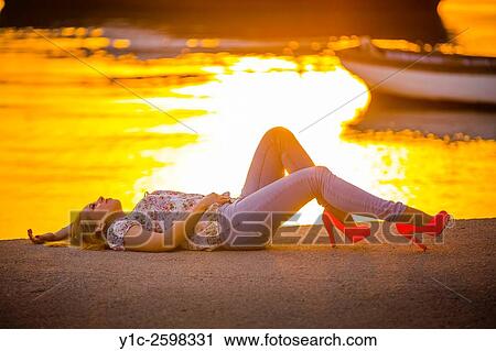 Stock Image - Teenager lying on back against bright sunset light. Fotosearch