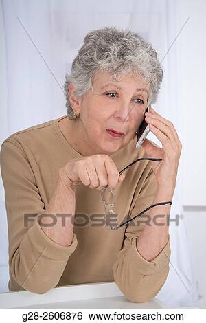 Thoughtful senior woman with grey hair, holding her glasses in her hand and using a mobile phone View Large Photo Image Stock Photograph - Thoughtful senior woman with grey hair, holding her glasses in her hand and using a mobile phone. Fotosearch