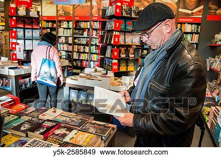 Stock Photo - Tilburg, Netherlands. Middle aged man reading a possible new book inside a bookstore.. Fotosearch