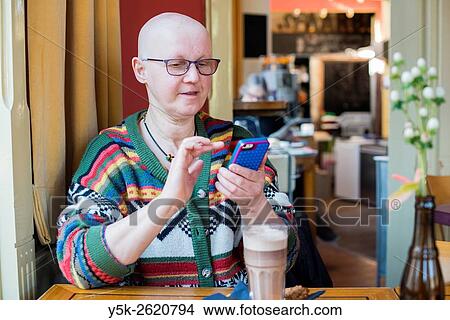Tilburg, Netherlands. Middle aged balding woman communicating with her smartphone while sitting in a cafe, drinking coffee. View Large Photo Image Picture - Tilburg, Netherlands. Middle aged balding woman communicating with her smartphone while sitting in a cafe, drinking coffee.. Fotosearch
