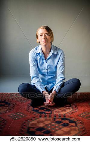 Stock Image - Tilburg, Netherlands. Studio shot of an attractive, blonde woman sitting on carpet.. Fotosearch