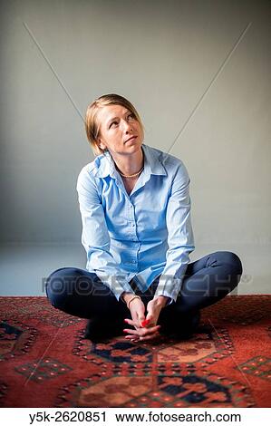 Stock Image - Tilburg, Netherlands. Studio shot of an attractive, blonde woman sitting on carpet.. Fotosearch