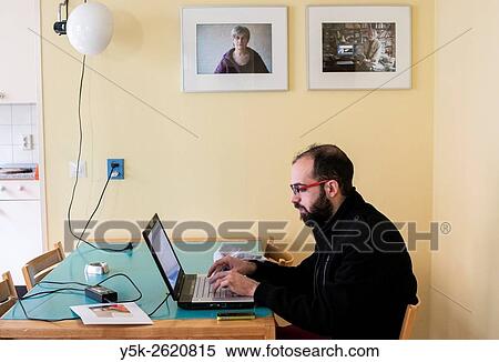 Tilburg, Netherlands. Syrian male refugee, working on his newly aquired laptop computer, while sitting on a dining room table. View Large Photo Image Stock Photography - Tilburg, Netherlands. Syrian male refugee, working on his newly aquired laptop computer, while sitting on a dining room table.. Fotosearch